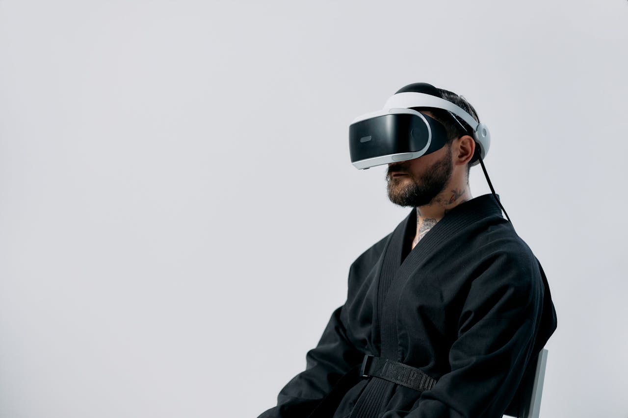 Bearded man in black attire using a VR headset against a plain white background in a studio.